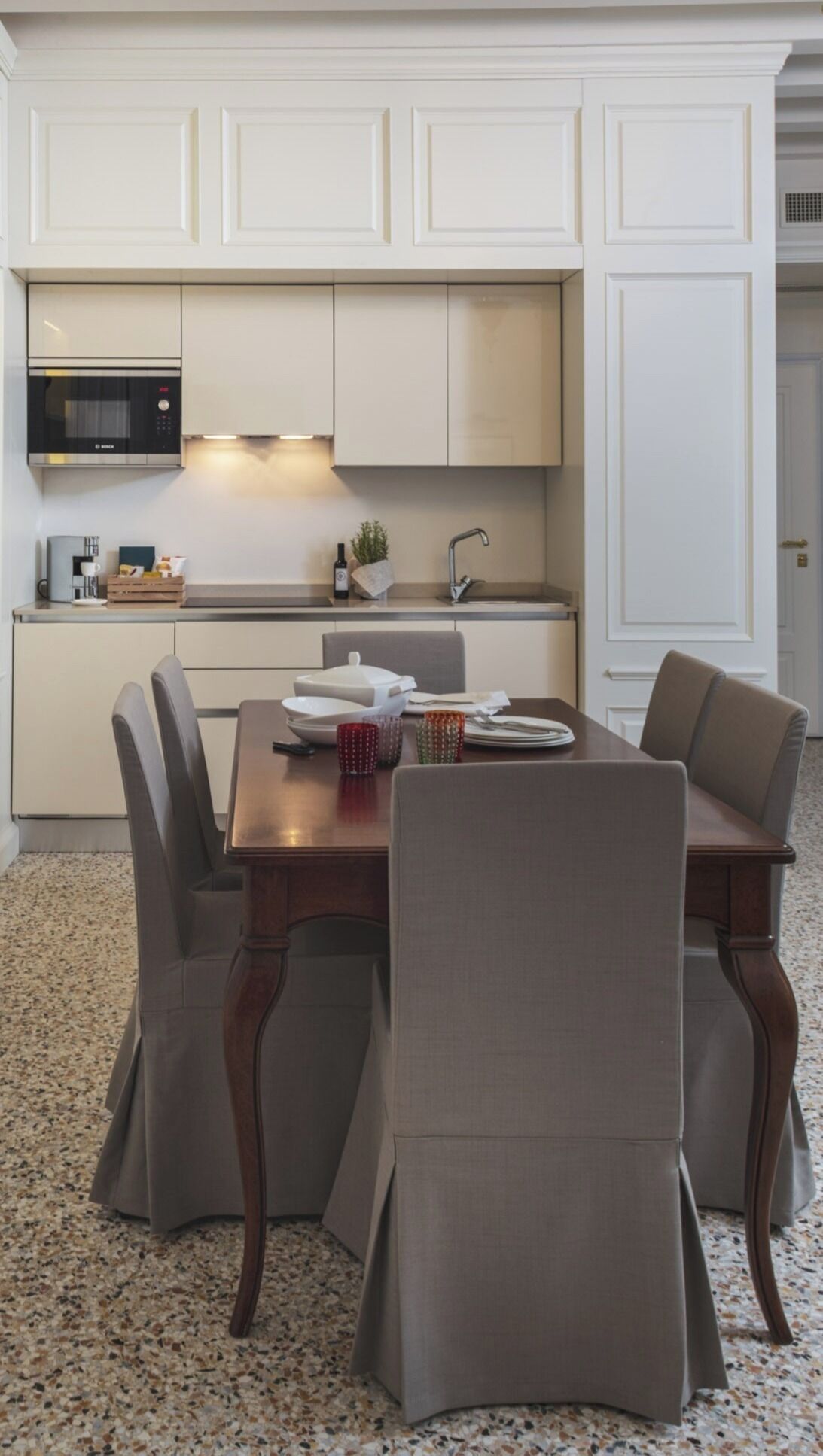 Une cuisine moderne avec des meubles blancs, un four à micro-ondes encastré et un coin repas comprenant une table en bois et quatre chaises.