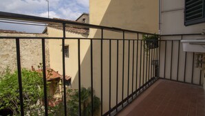 A narrow outdoor corridor with a tiled floor, a black metal railing, and a yellow building with a tiled roof. - Porcellana Art (Florence)