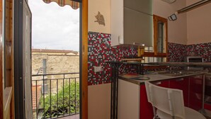 A kitchen with a red and white tiled backsplash, a white chair, and a view of a building outside. - Porcellana Art (Florence)