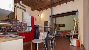 A kitchen with red cabinets, a white refrigerator, and a tiled backsplash. There are three metal bar stools and a wooden ladder leaning against the wall. - Porcellana Art (Florence)