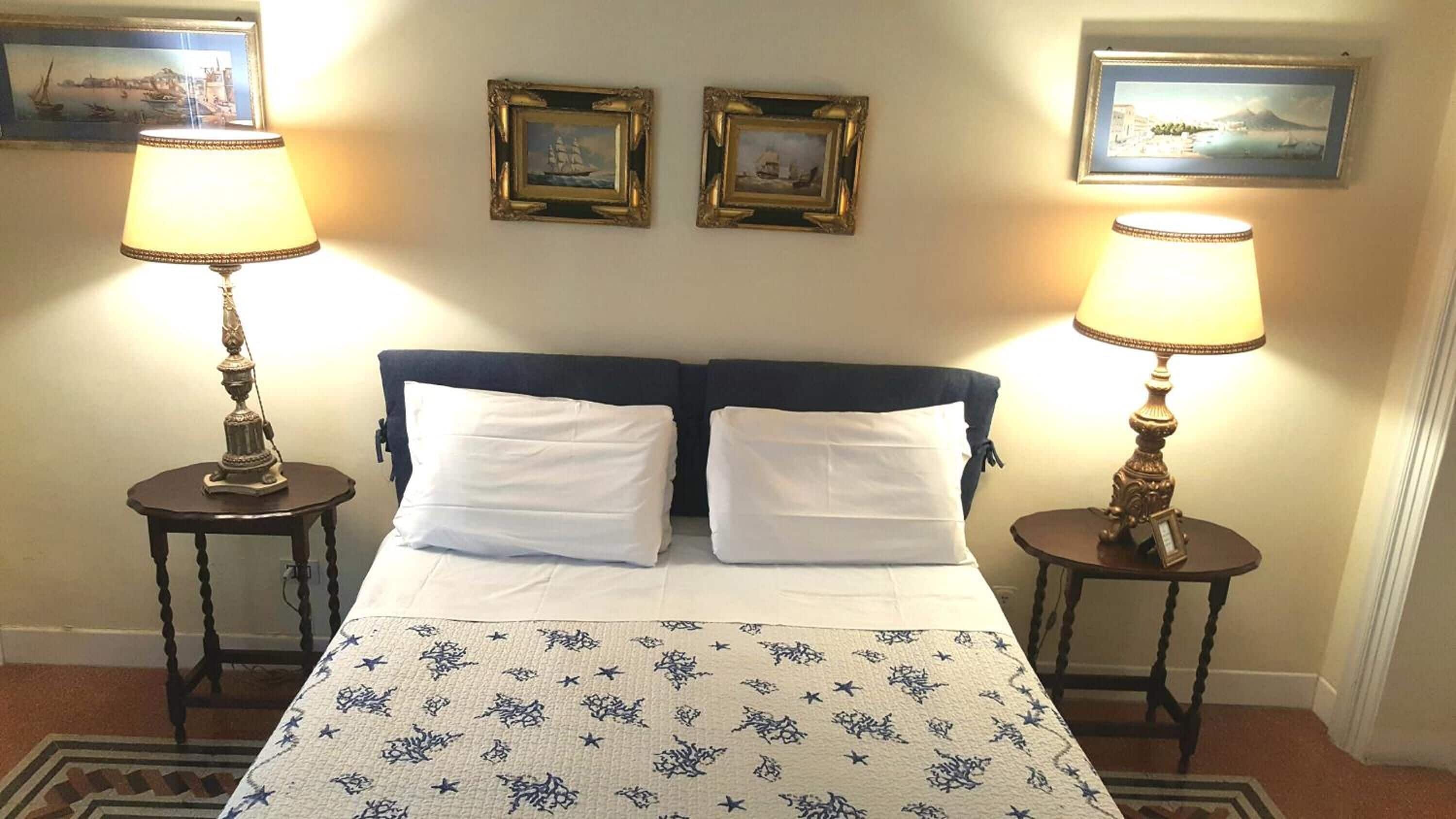 Ein Hotelzimmer mit einem Doppelbett, zwei Nachttischen mit Lampen und drei gerahmten Bildern an der Wand.