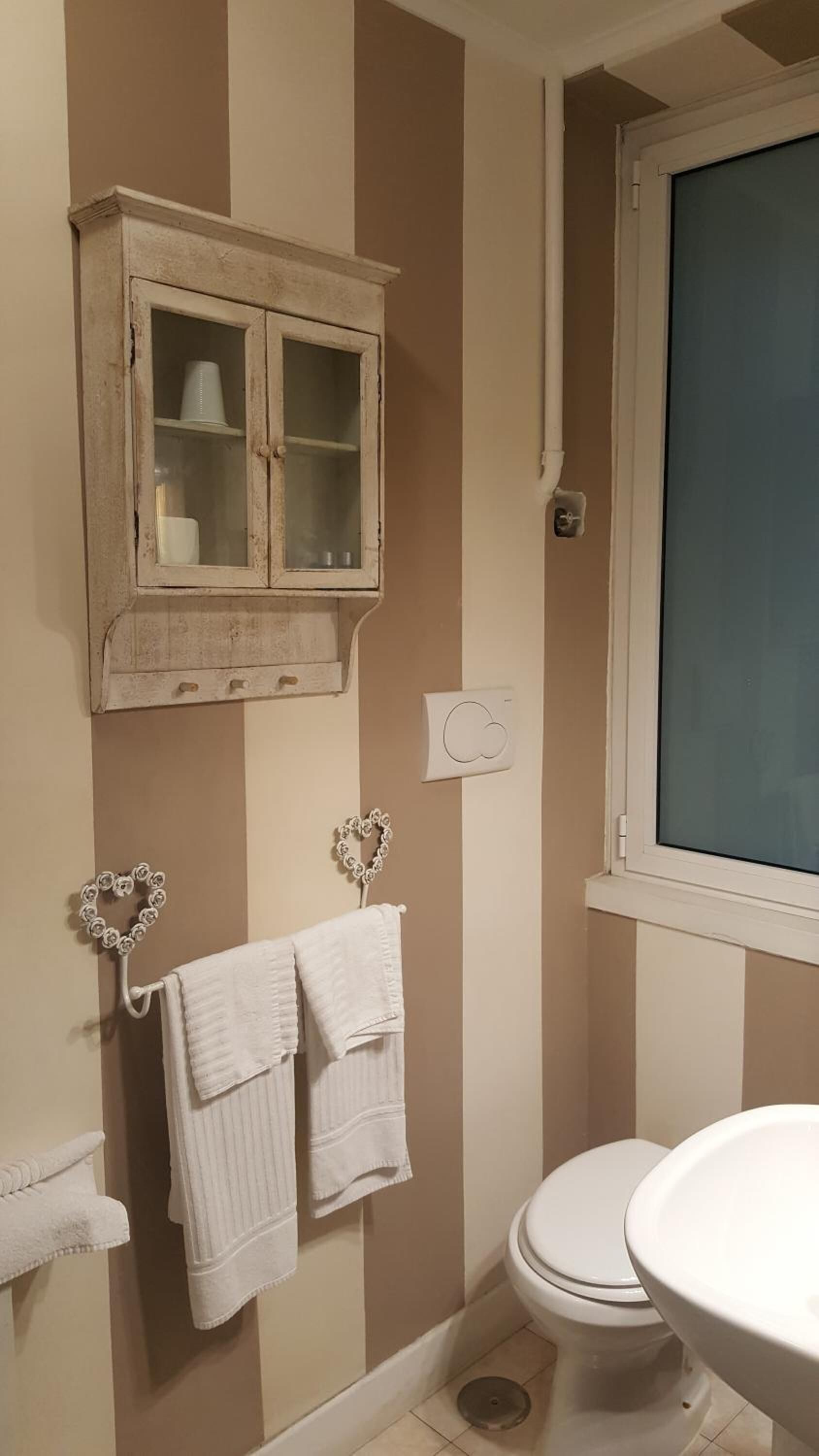 A bathroom with striped walls, a white toilet, a white sink, and a wooden cabinet with glass doors.