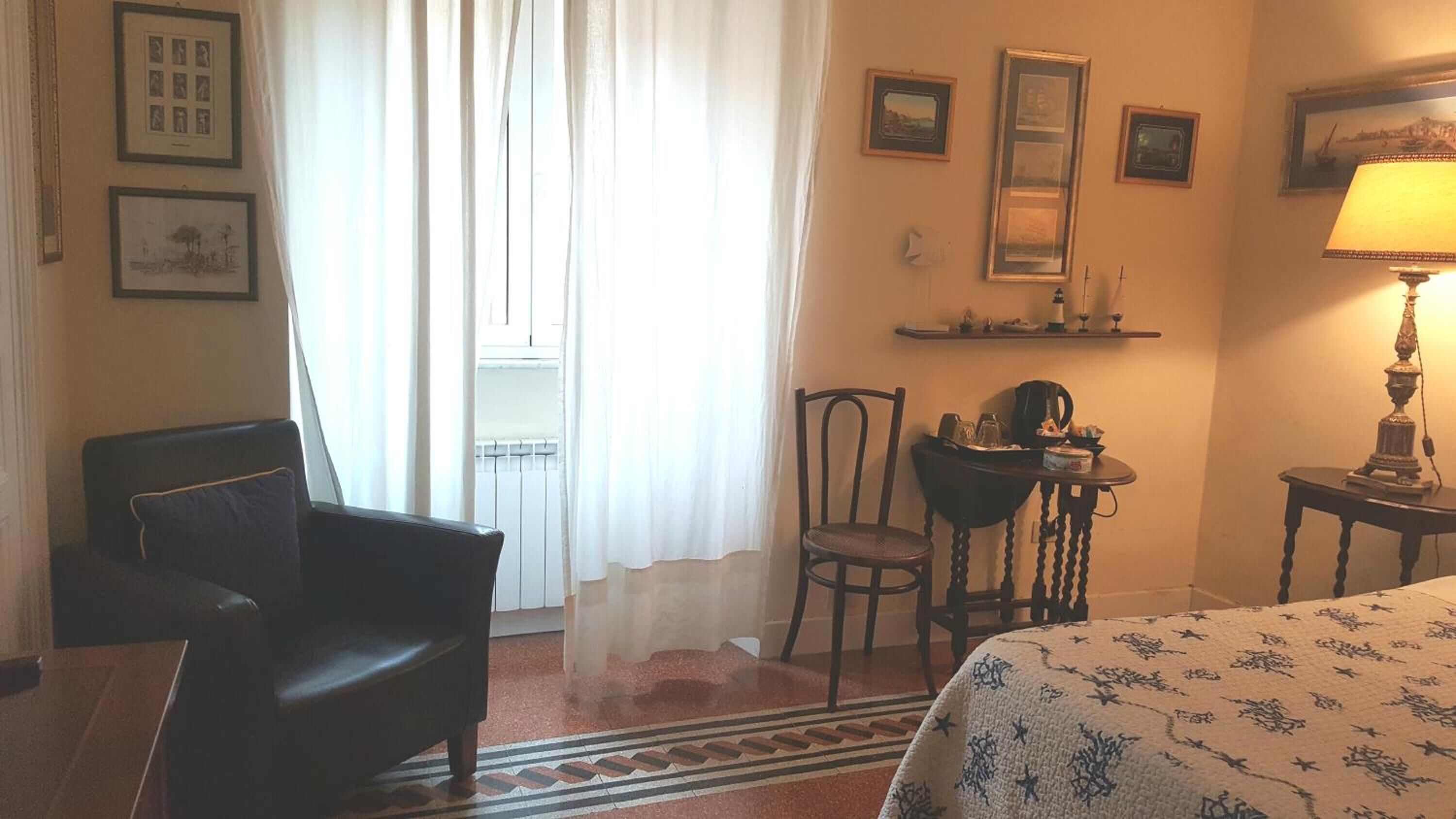 A hotel room with a bed, a chair, a desk with a lamp, and a window with curtains.