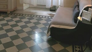 Una habitación con piso a cuadros, una cama con almohada, una lámpara, un espejo y una ventana con cortinas.