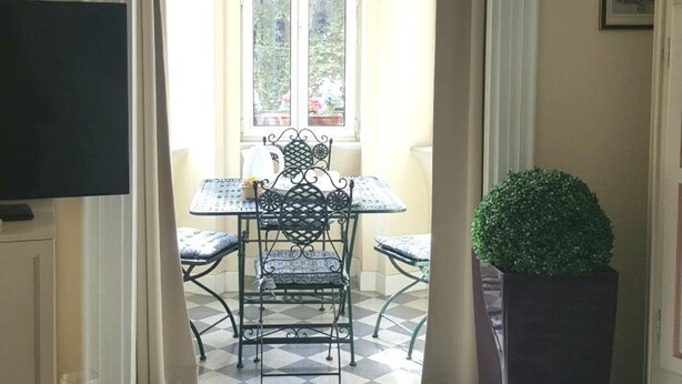 Una habitación con suelo a cuadros, una mesa de comedor con sillas, un televisor en un mueble y una planta grande en maceta.