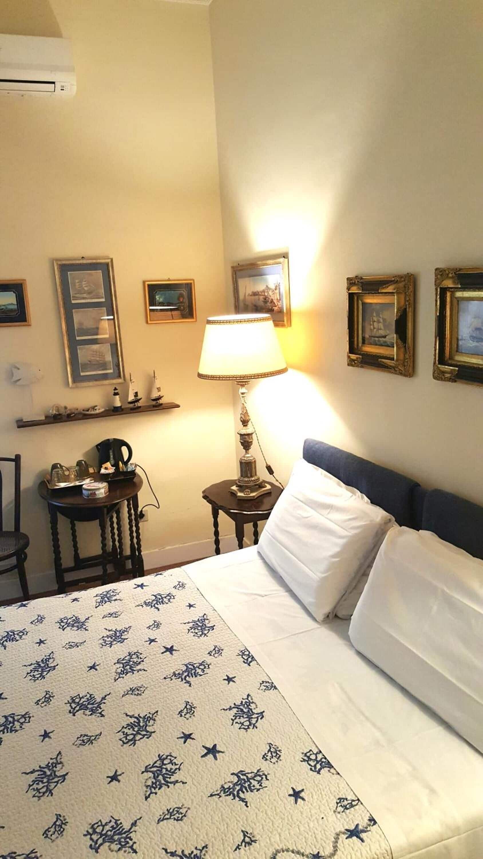 Una camera d'albergo con un letto, una scrivania con una lampada e diverse foto incorniciate appese al muro.