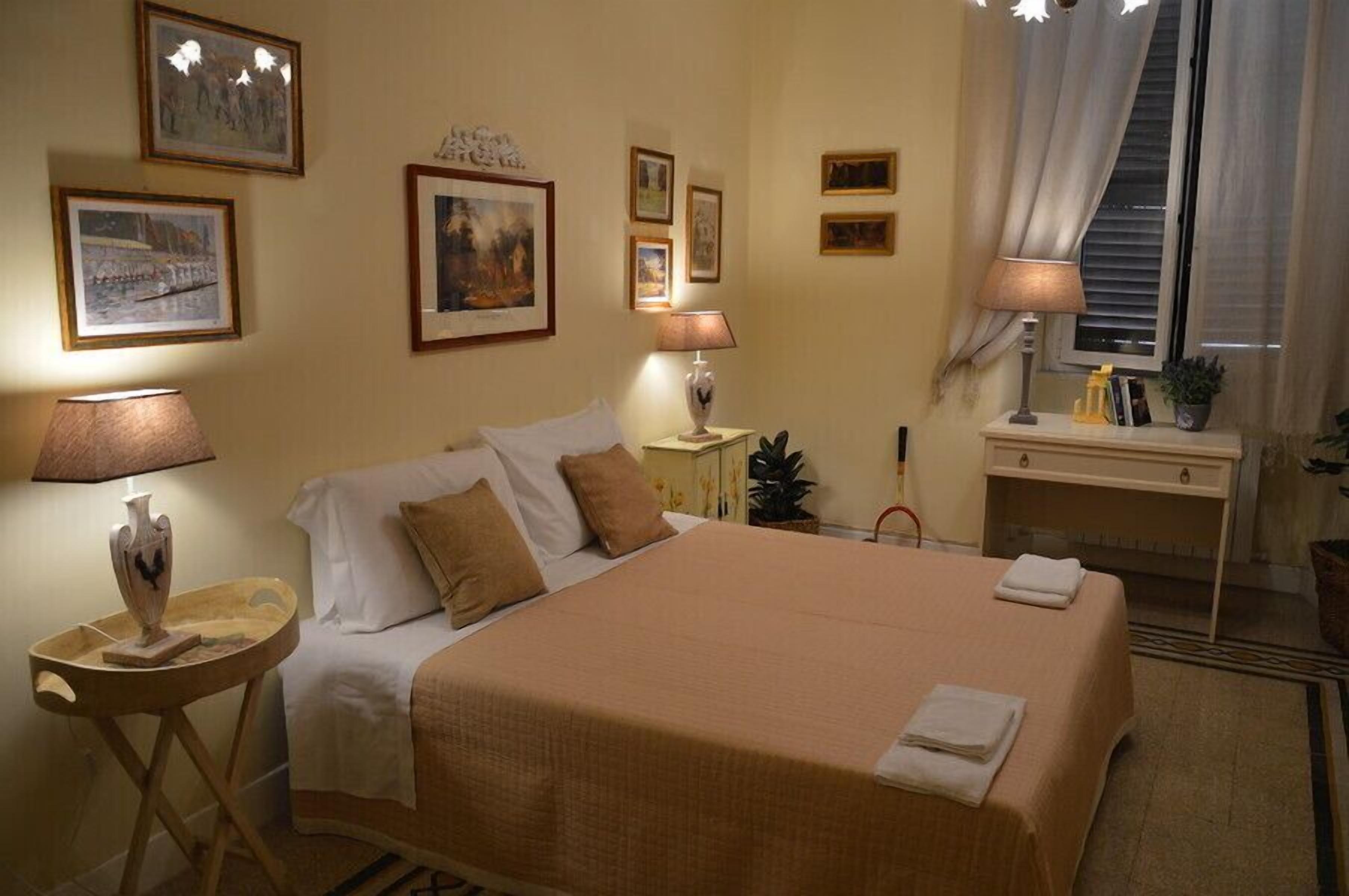 A neatly arranged hotel room with a large bed, bedside lamps, a small table with a vase, and framed pictures on the wall.