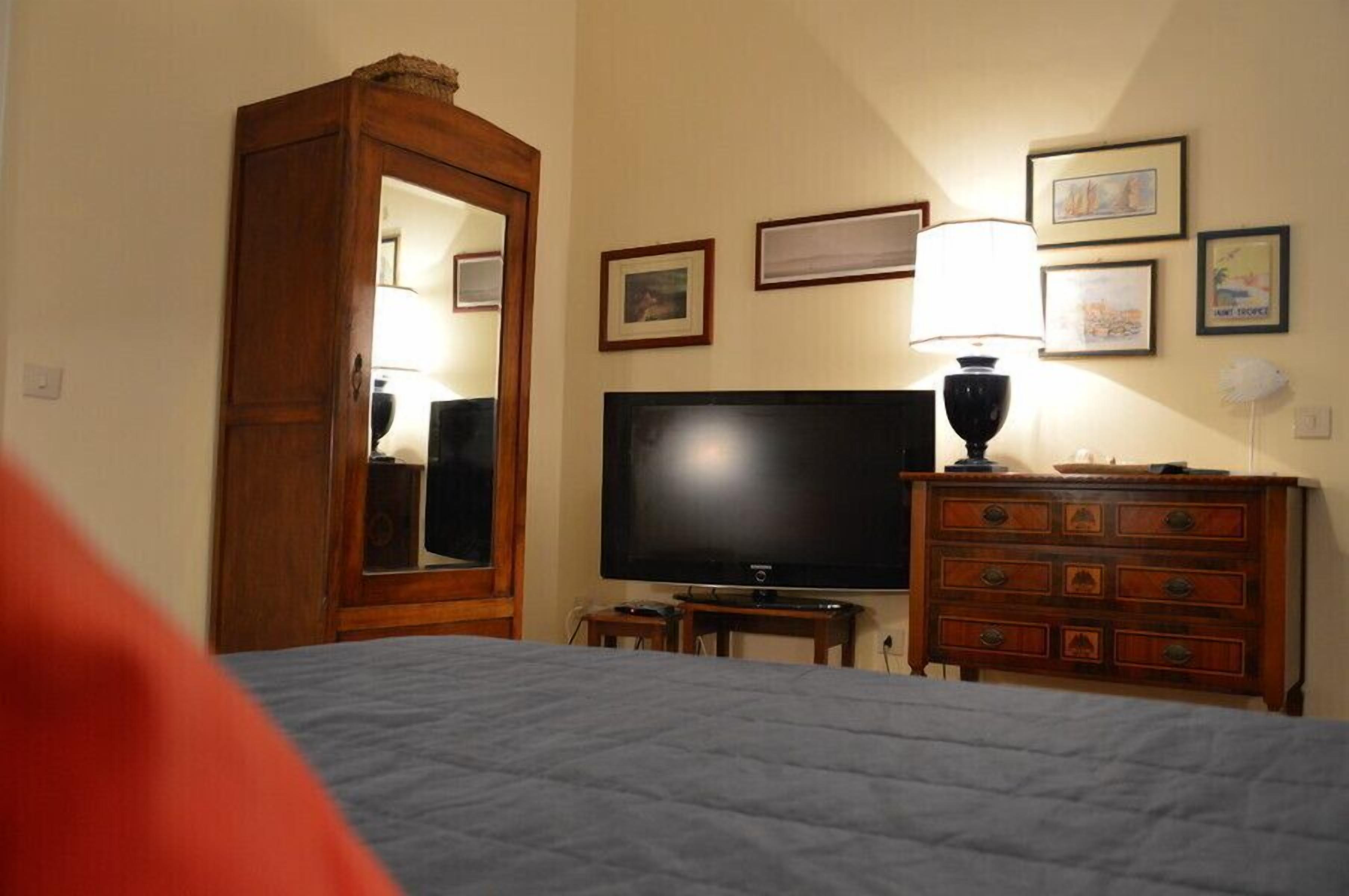 A hotel room with a bed, a television, a dresser, and framed pictures on the wall.