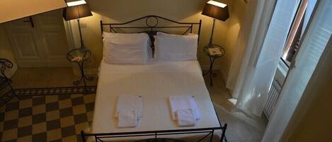 A neatly made bed with white linens and towels, two bedside lamps, and a checkered floor.