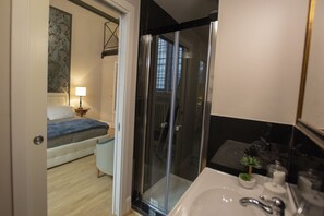 A modern bathroom with a glass shower enclosure, a white sink, and a small plant on the counter.