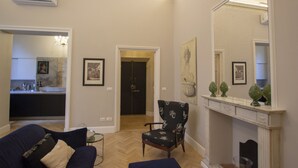 Una sala de estar con un sofá azul oscuro, un sillón estampado, una chimenea y un espejo grande.