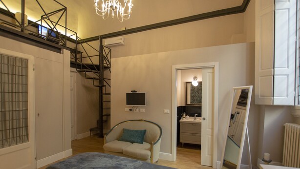 Un dormitorio con cama, una silla, un escritorio, un espejo y una escalera.