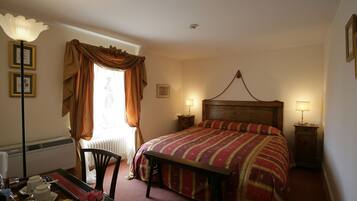 A bedroom with a large bed, two bedside tables, a wooden headboard, a desk with a chair, and a radiator.