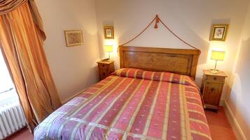 A bedroom with a wooden headboard, a bed with a patterned bedspread, two bedside tables with lamps, and a window with curtains.
