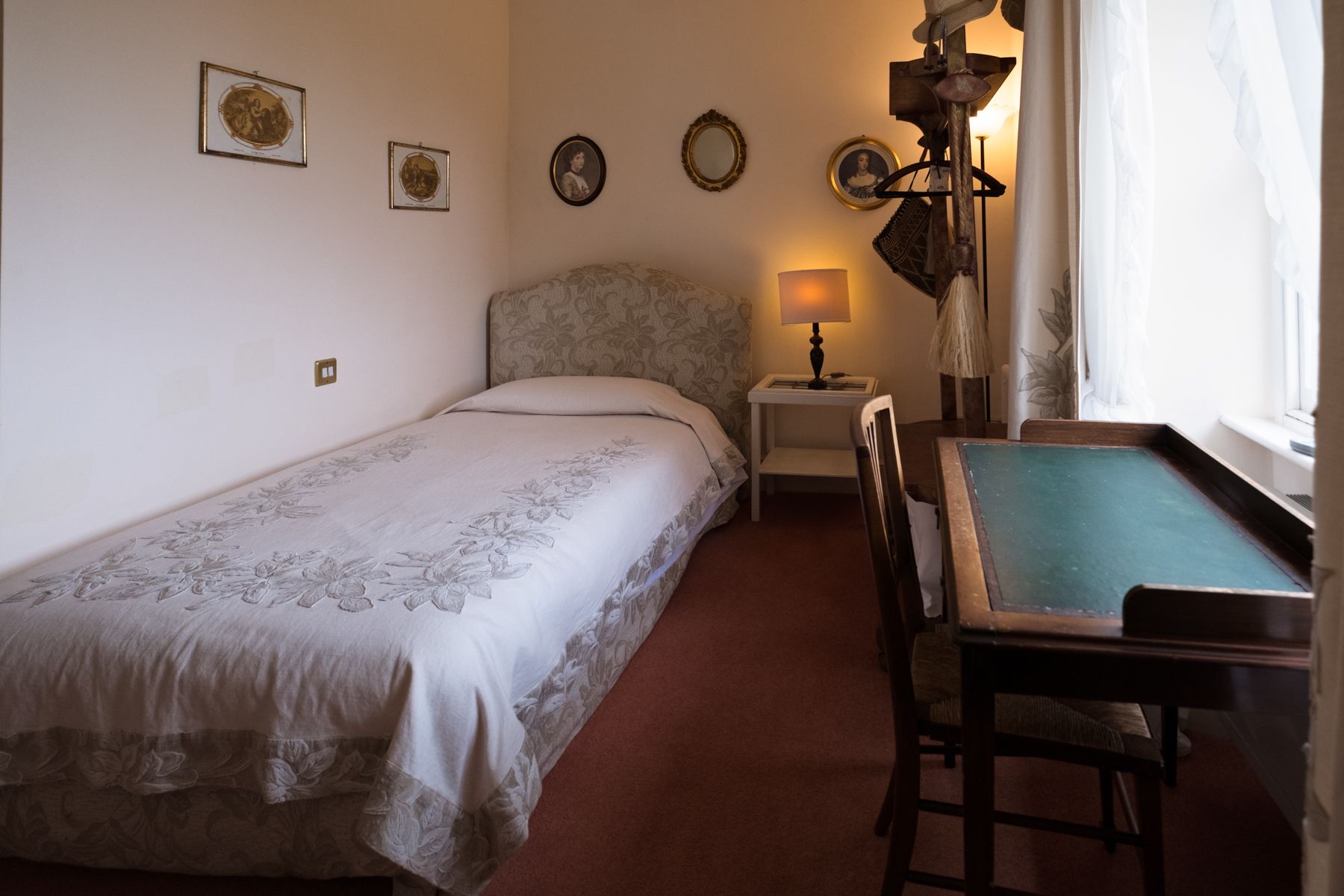 A single bed with floral bedding, a small bedside table with a lamp, and a billiards table.