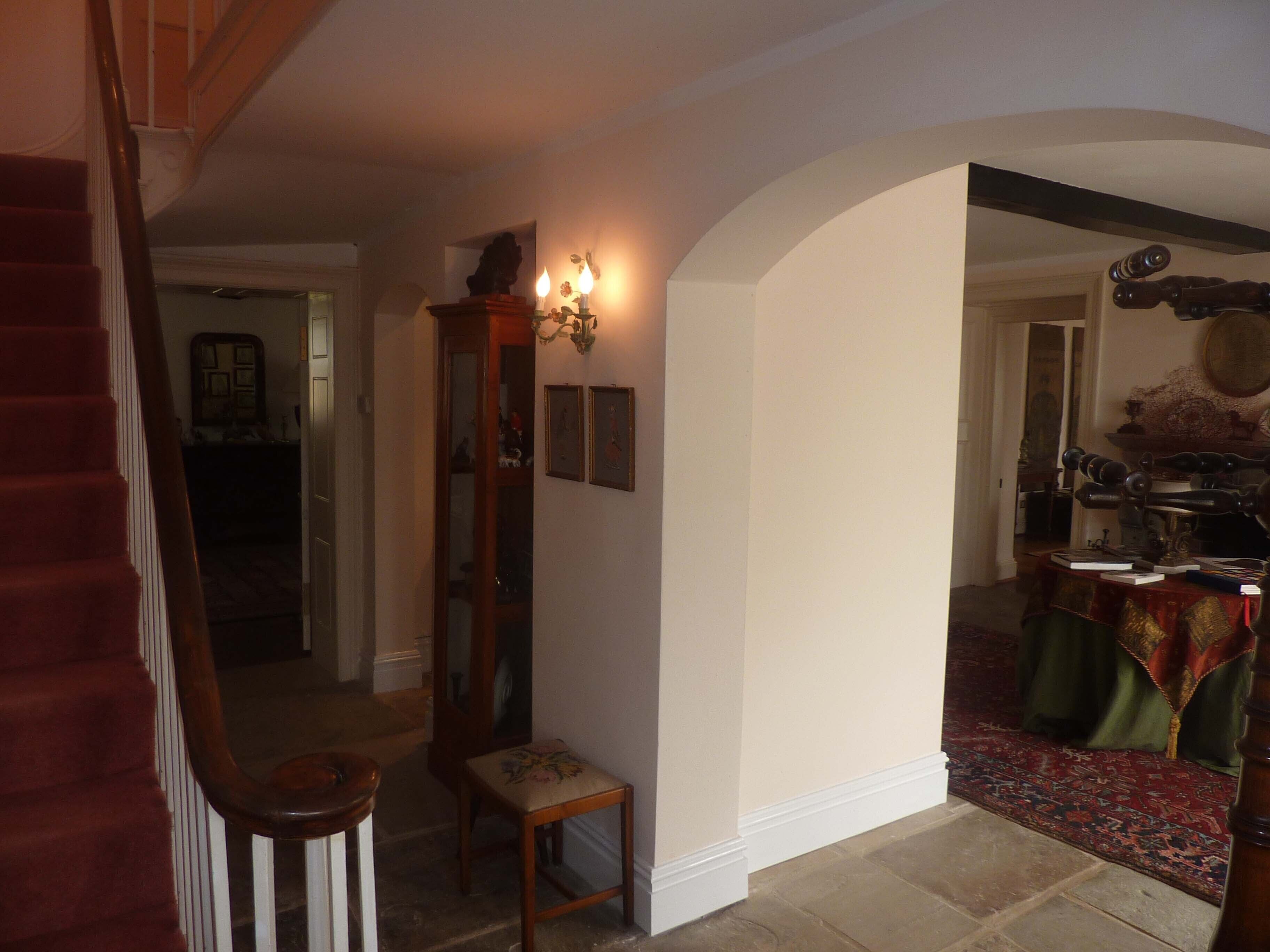 Una escalera conduce a una habitación con una araña, un espejo y una mesa cubierta con un mantel verde.