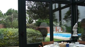 An indoor dining area with a view of a swimming pool and a brick building. - Brampton Grange (Northampton)