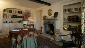A cozy room with a fireplace, bookshelves, a table with a quilt, and a chair. - Brampton Grange (Northampton)