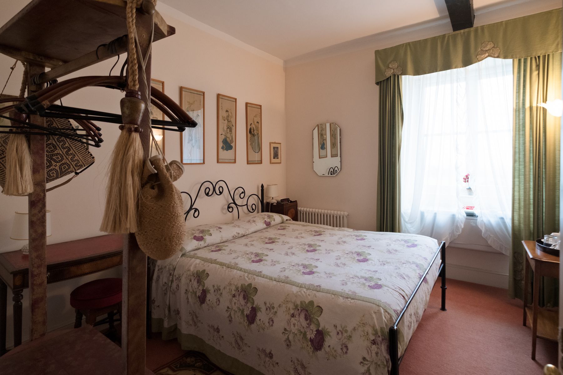 A bedroom with a bed, a desk, a chair, a hanging bag, and a mirror on the wall.