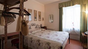 A bedroom with a bed, a desk, a chair, a hanging bag, and a mirror on the wall.