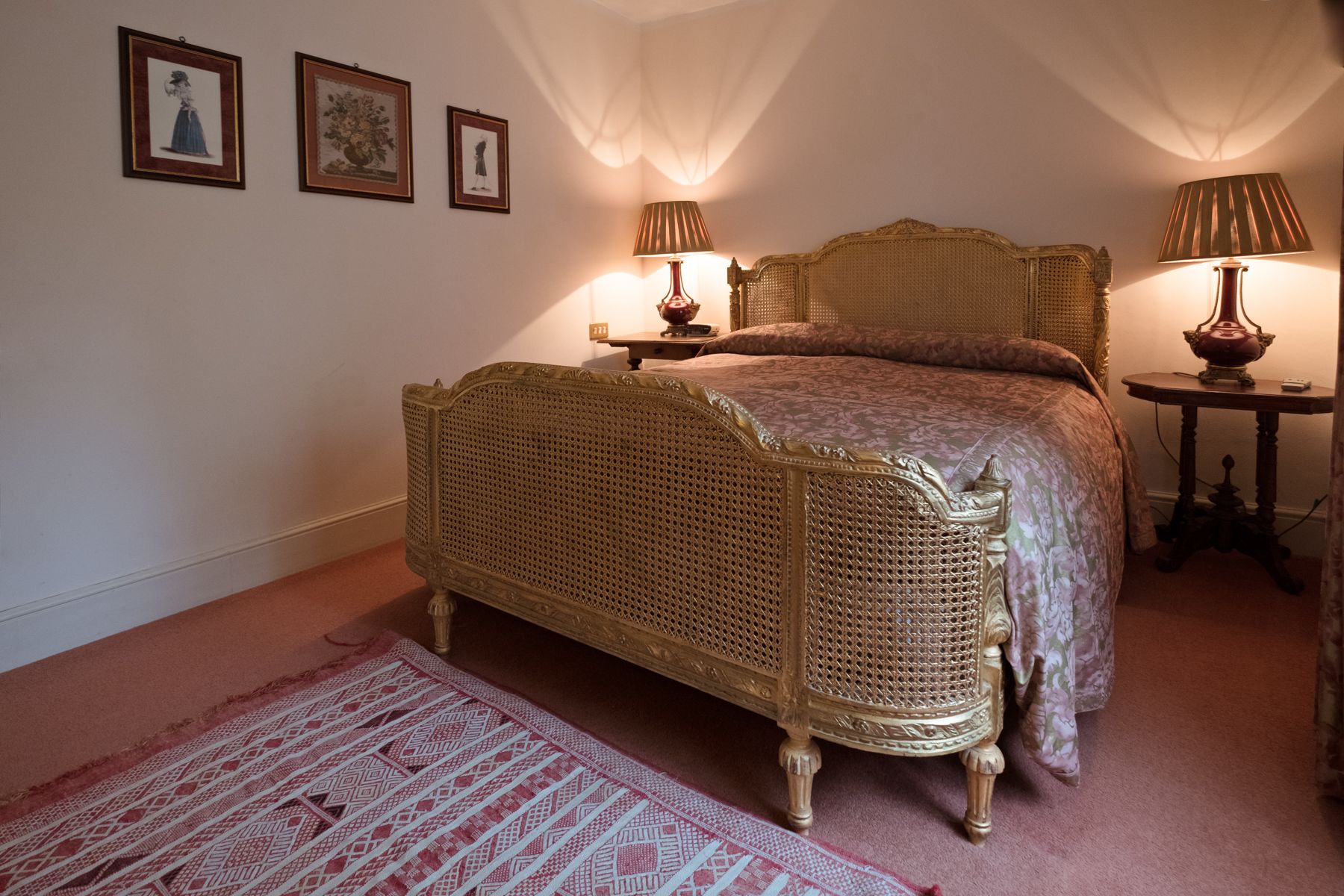 A bedroom with a large ornate bed, two bedside tables with lamps, and three framed pictures on the wall.