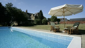 A swimming pool with a tiled edge, a lounge area with wicker chairs and a table, and a white umbrella. - Brampton Grange (Northampton)