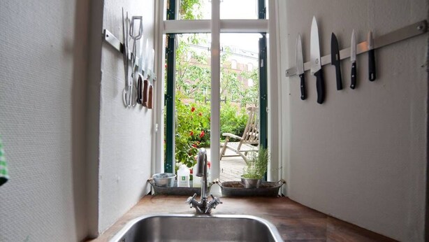 Una cocina con un lavaplatos de acero inoxidable, una ventana con vista a un jardín y un organizador de cuchillos en la pared.