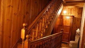 A wooden staircase with a handrail, a rug on the floor, and a chair in a room with wooden walls and a cabinet.