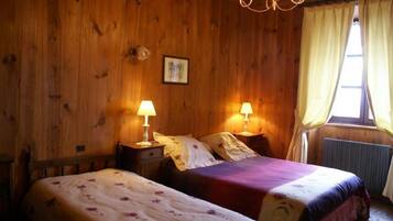 A wooden room with two beds, each with a bedside table and lamp, a window with curtains, and a chandelier.