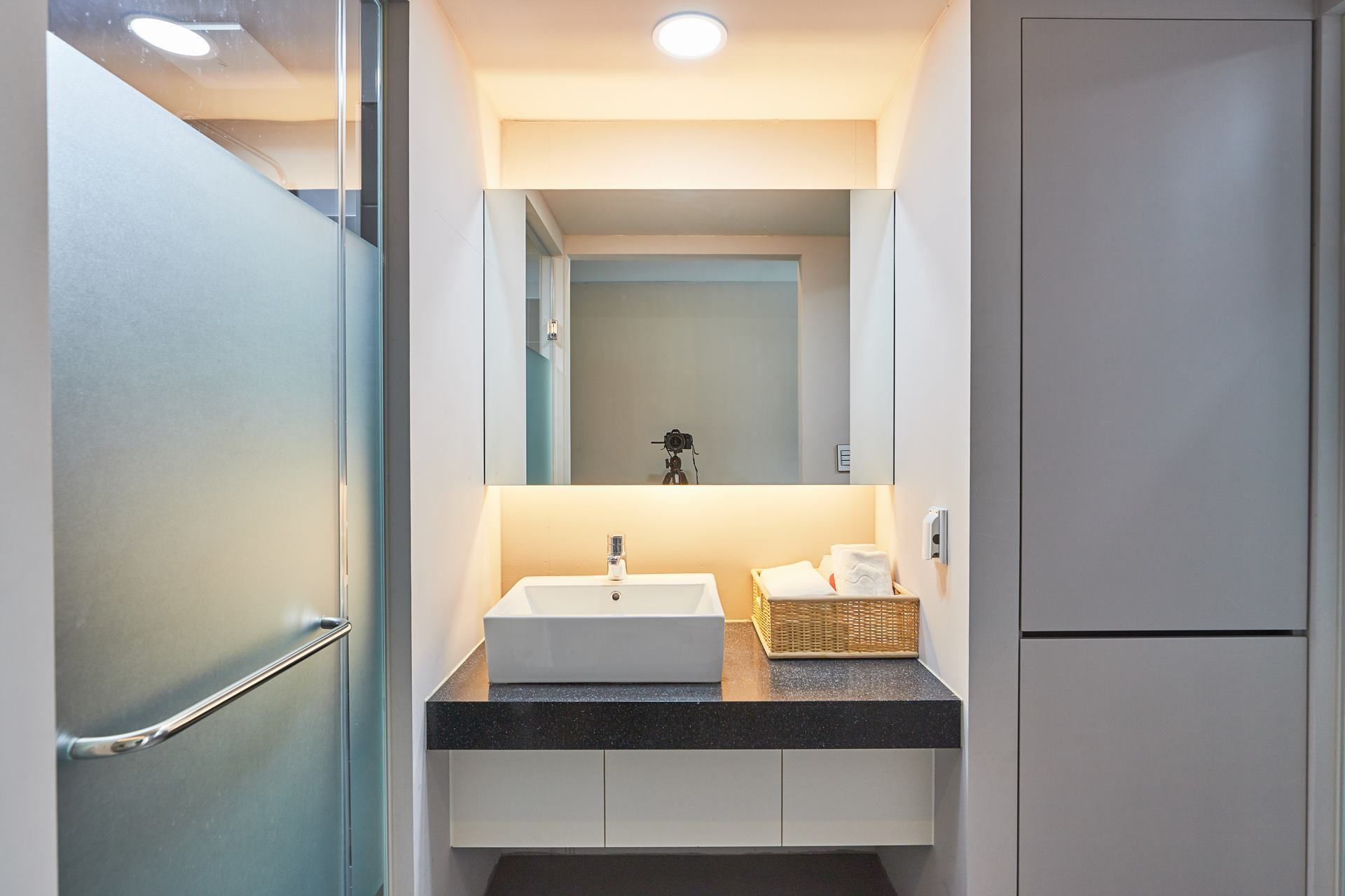 A modern bathroom with a white sink, a mirror, and a camera on a tripod.