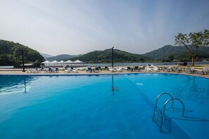 A swimming pool with lounge chairs and umbrellas, surrounded by mountains and a clear sky. - Parotia Water House (Gapyeong)
