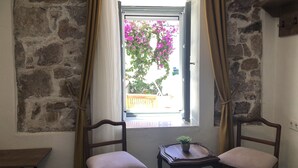 A room with a stone wall, a window with a curtain, two chairs, and a small table with a plant. - Kastoria Butik Pansiyon (Ayvalik)