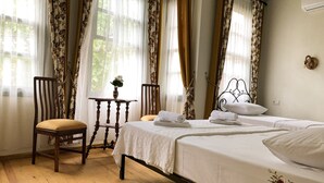 A bedroom with a bed, a chair, a small table with a vase, and curtains. - Kastoria Butik Pansiyon (Ayvalik)