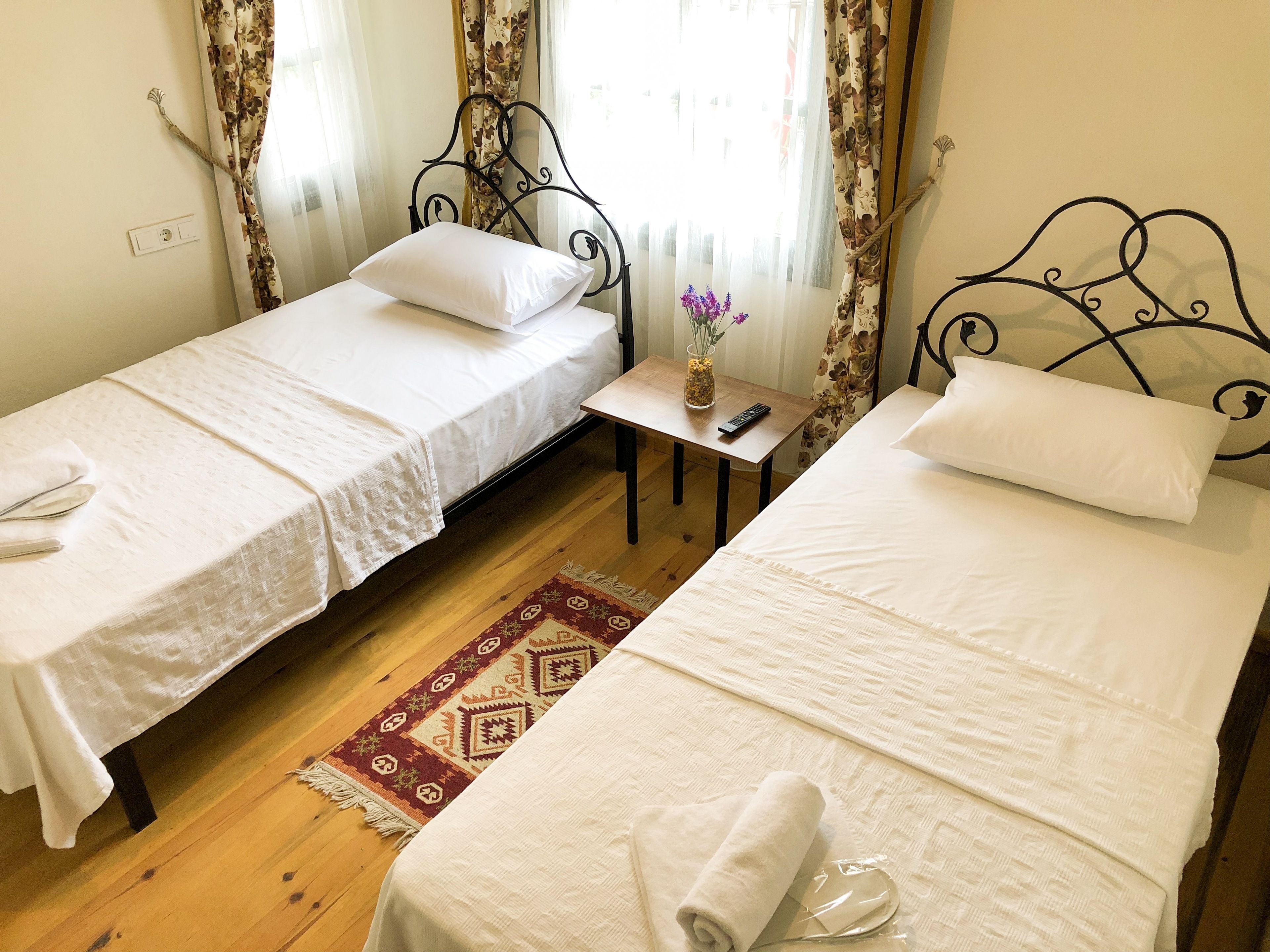A hotel room with two single beds, a small table with a vase of flowers, and a wooden floor.