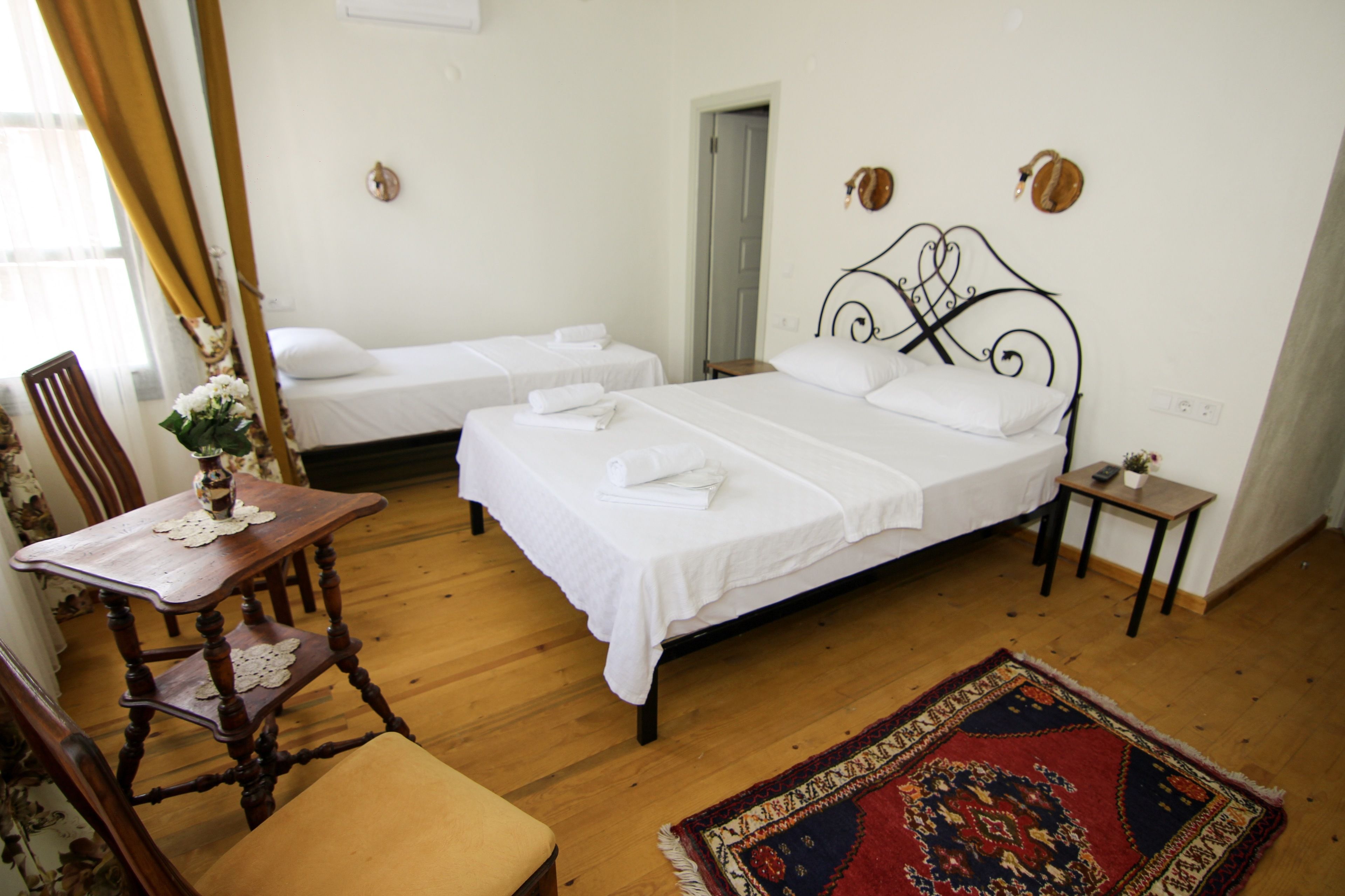 A hotel room with two single beds, a wooden chair, a small table with a vase, and a decorative rug.