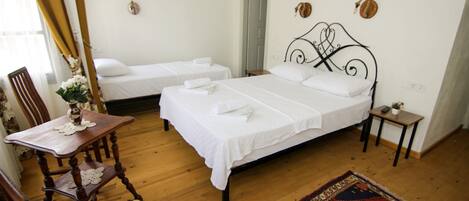 A hotel room with two single beds, a wooden chair, a small table with a vase, and a decorative rug.