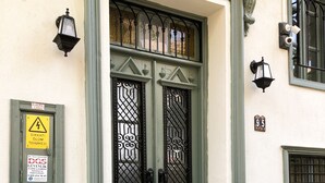 A green double door with decorative ironwork, a yellow warning sign, and a small number plaque. - Kastoria Butik Pansiyon (Ayvalik)