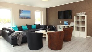 A modern living room with a sectional sofa, a coffee table, and a TV mounted on the wall. - Villa Thormarcon (Malchow)