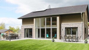 A modern two-story building with large windows, a patio with outdoor seating, and a well-maintained lawn. - Villa Thormarcon (Malchow)