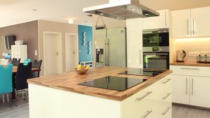 A modern kitchen with a central island, stainless steel appliances, and a dining area with chairs and a table. - Villa Thormarcon (Malchow)