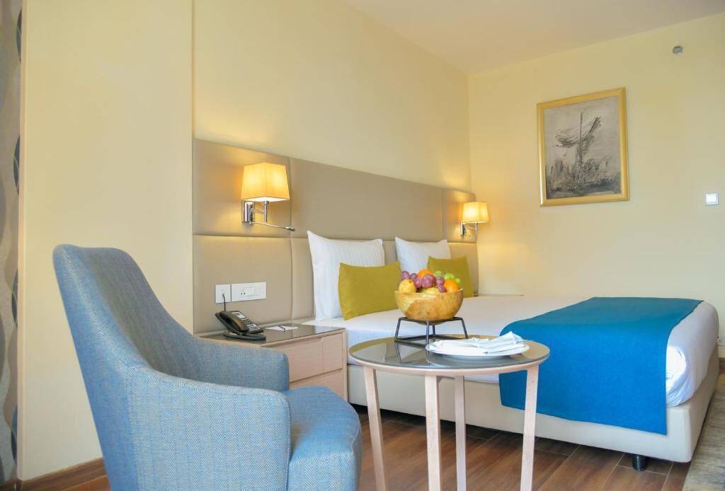Una habitación de hotel con una cama, una silla, una mesita y dos lámparas de noche.