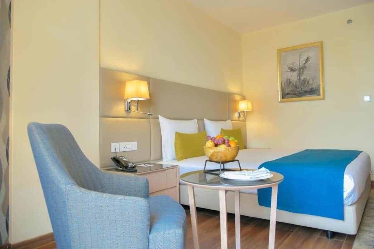 Una habitación de hotel con una cama, una silla, una mesita y dos lámparas de noche.