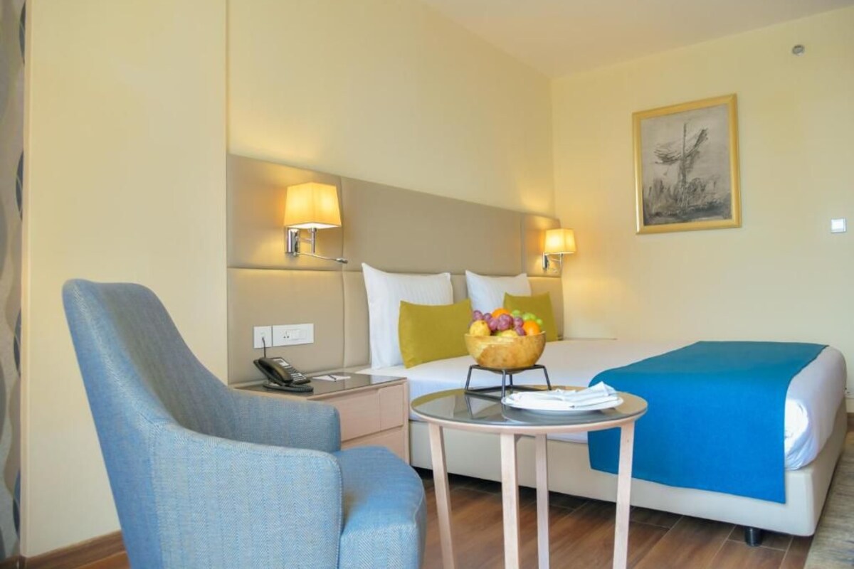 Una habitación de hotel con una cama, una silla, una mesita y dos lámparas de noche.