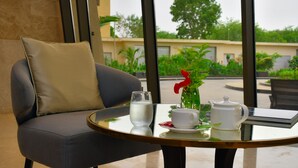 Una habitación moderna con un sofá, una mesa de vidrio con tetera, taza y vaso, y vista a áreas verdes al exterior.