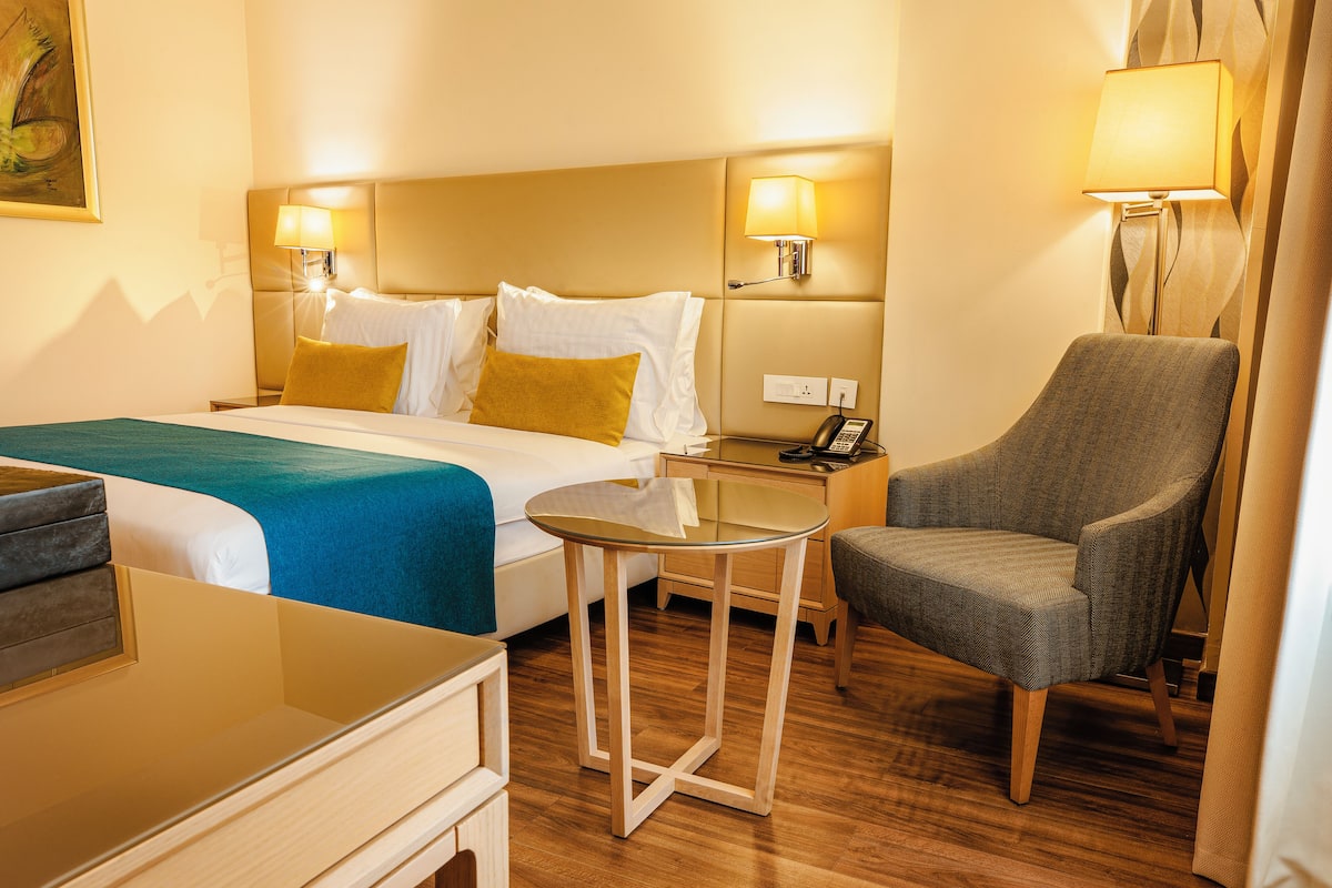 Una habitación de hotel con una cama, una silla, una mesita y dos lámparas de noche.