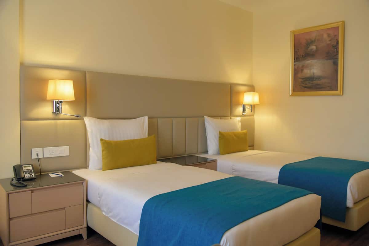 Habitación de hotel con dos camas, lámparas de noche, una mesita de noche con teléfono y un cuadro en la pared.