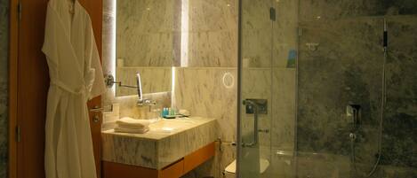Een moderne badkamer met een marmeren wastafelmeubel, een douche met glazen wanden en een badjas hangend aan een deur.