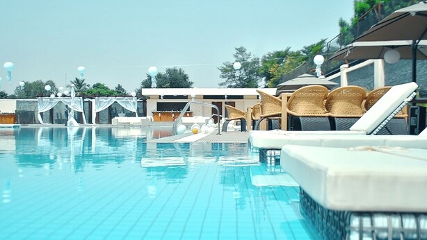 Una piscina con sillones de baño y sombrillas, rodeada por un edificio con una zona cubierta.
