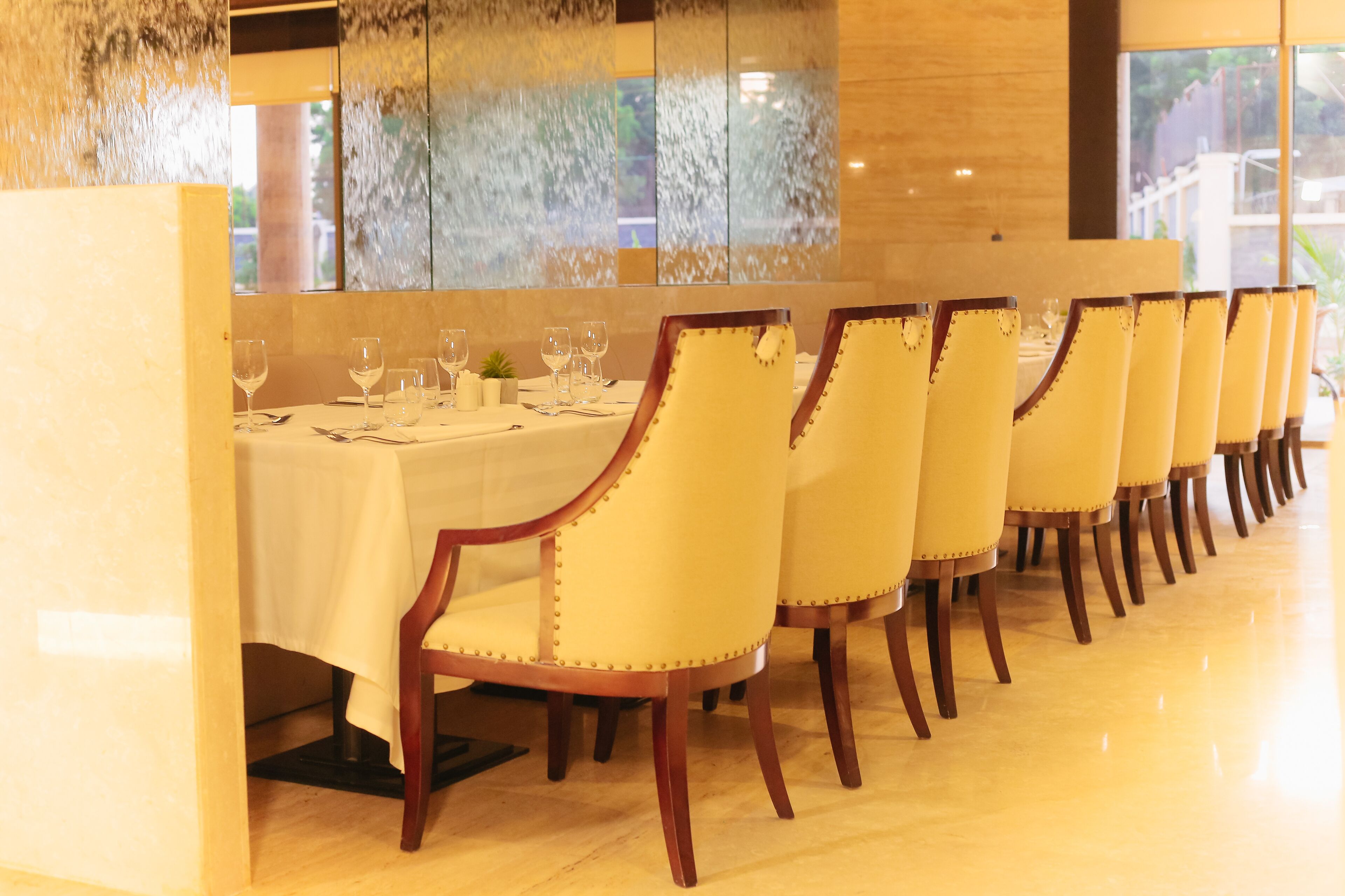 A dining area with a long table set for multiple guests, featuring chairs with a classic design and a white tablecloth.