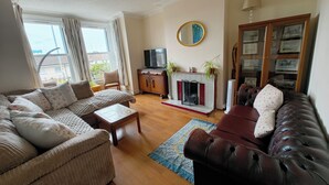 Una sala de estar con sofá, sillón de cuero, chimenea, televisor y ventana con cortinas.